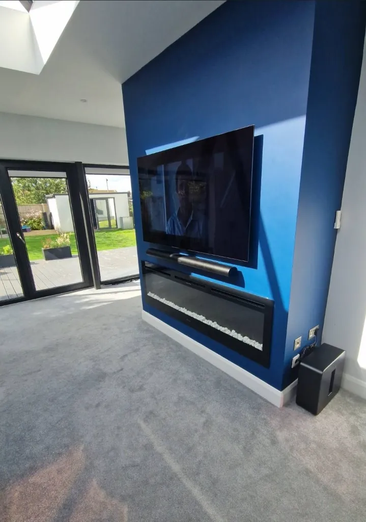 TV, soundbar and inset fire on a blue feature wall, with a subwoofer in the corner